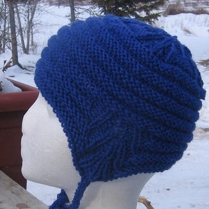Puede incluir: Un gorro azul de punto con una larga corbata. El gorro está hecho con un patrón de punto texturizado y tiene un diseño simple.