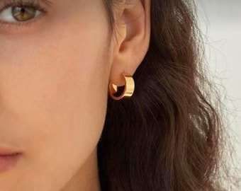 Op de afbeelding: Een close-up van iemands oor met een gouden oorring. De oorring is simpel en elegant, met een gladde, gepolijste afwerking.
