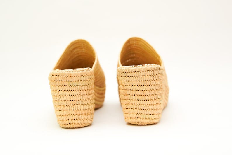 May include: Two pairs of woven raffia slip-on sandals. The open-toe shoes have a natural beige color and a textured, basket-weave design. The shoes are set against a white background.