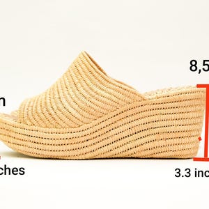 May include: A woven raffia wedge sandal in a natural beige color. The sandal has an open toe design and a wedge heel that measures 3.3 inches (8.5 cm) high. The platform is 1.5 inches (4 cm) high. The sandal is a slip-on style.