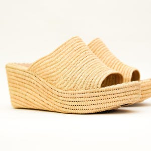 May include: A pair of beige woven wedge sandals. The open-toe shoes have a thick, curved sole and a woven strap that covers the top of the foot. The sandals are made of a light-colored, natural material.