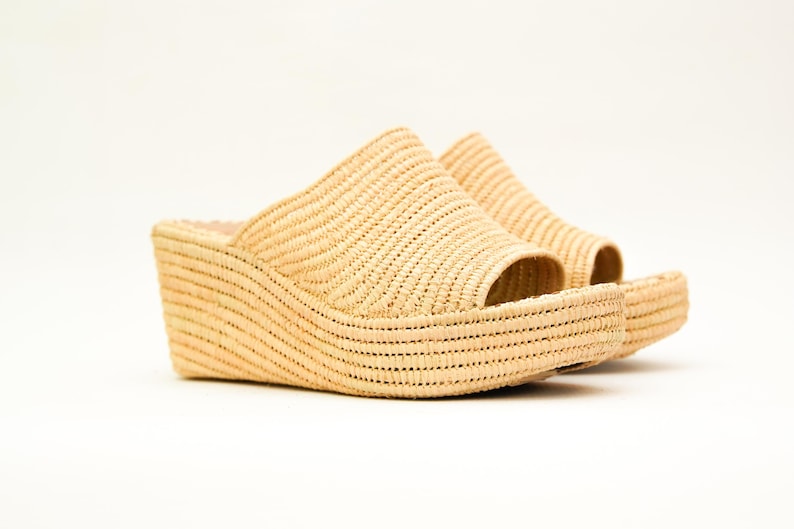 May include: A pair of beige woven wedge sandals. The open-toe shoes have a thick, curved sole and a woven strap that covers the top of the foot. The sandals are made of a light-colored, natural material.