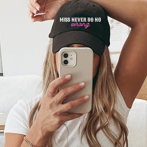May include: A black baseball cap featuring the white embroidered text MISS NEVER DO NO and the pink embroidered word wrong. The cap has a curved brim and a structured crown, displaying a clear and legible design on the front panel.