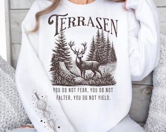 May include: White sweatshirt with a brown graphic of a deer in a forest with the text "TERRASEN" above the deer and "YOU DO NOT FEAR, YOU DO NOT FALTER, YOU DO NOT YIELD." below the deer.