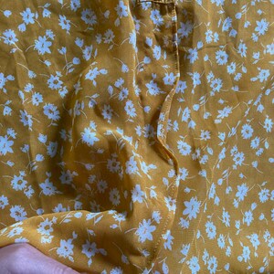 May include: A yellow sheer blouse with a white floral pattern. The blouse has a button closure at the neck.