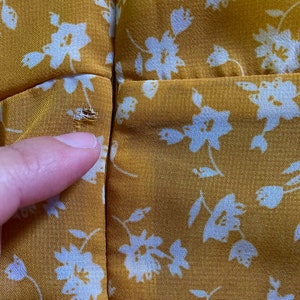 May include: Close-up of a yellow fabric with a white floral pattern. The fabric has a small hole near the seam.