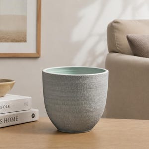May include: A rounded planter with a textured grey exterior and a smooth, light mint green interior. The vessel has a wide, open top and a tapered base, showcasing a distinct contrast between the rough outer surface and the soft-coloured inner lining.