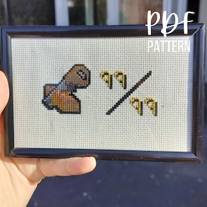 Può includere: Un ricamo a punto croce incorniciato con un personaggio marrone e oro con il testo "99/99" in filo dorato.