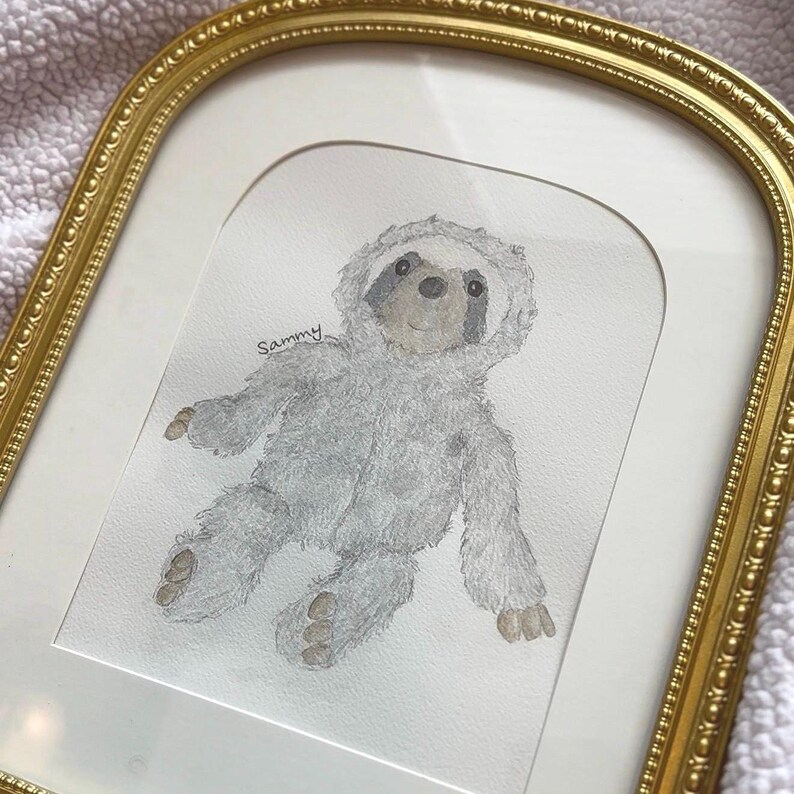 May include: Watercolor painting of a gray sloth wearing a hooded outfit, framed in a gold ornate frame. The sloth has a light gray body, a darker gray face, and brown feet. The name "Sammy" is written above the sloth.