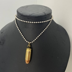 Op de afbeelding: Een zilveren kogelketting met een messingkleurige kogelhanger. De kogel heeft een koperkleurige punt. De ketting wordt getoond op een zwarte mannequin.
