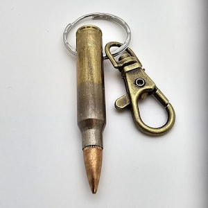 Puede incluir: Un llavero de casquillo de bala de latón con un anillo de llave de plata y un cierre giratorio de latón.