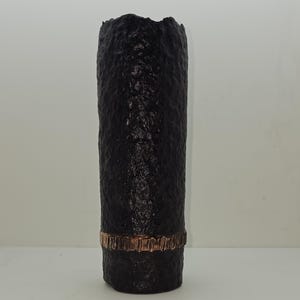 Puede incluir: Jarrón de cerámica negro con una superficie texturizada y una banda de cobre alrededor del centro.
