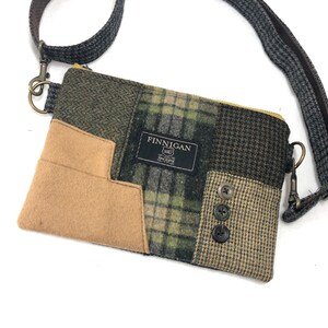 May include: A small, brown, green, and black patchwork crossbody bag with a zipper closure and a brown and gray strap. The bag has a label that says "FINNIGAN" on it.