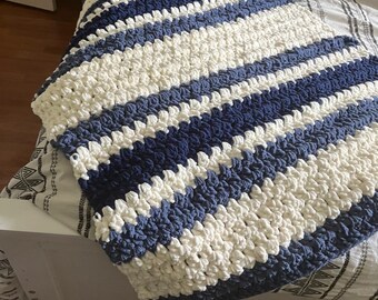 Könnte beinhalten: Eine gestrickte weiße und blaue gestreifte Decke mit einem strukturierten, bauschigen Design.