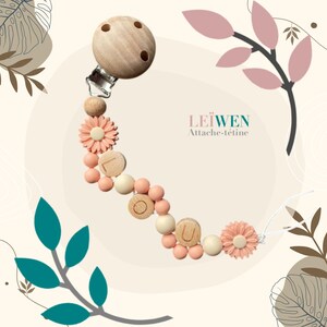 May include: A pink and white silicone and wooden baby teether with a wooden clip. The teether has a flower charm and wooden beads that spell out "LOVE".