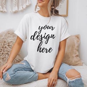 Può includere: Una maglietta bianca con il testo "your design here" scritto in corsivo nero.