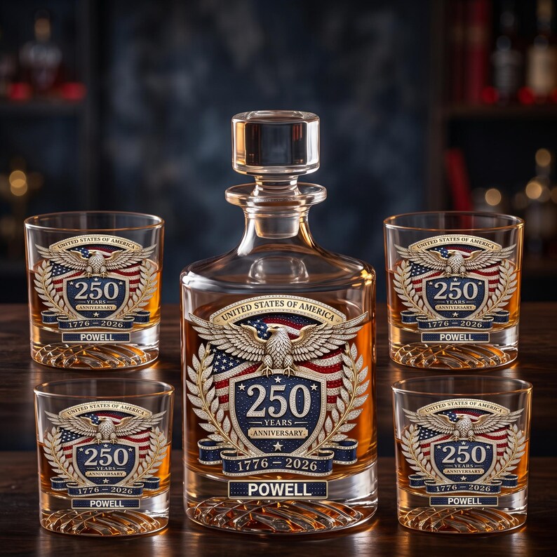 May include: A clear glass decanter and four matching whiskey glasses, each featuring an etched design of a bald eagle, the American flag, and the text United States of America 250 Years Anniversary 1776-2026 with the name Powell printed below.
