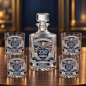 May include: A clear glass decanter and four matching glasses featuring a United States of America 250 years anniversary emblem with an eagle, American flag, and the text 1776-2026 and POWELL. The glassware has a textured base and a clear stopper.