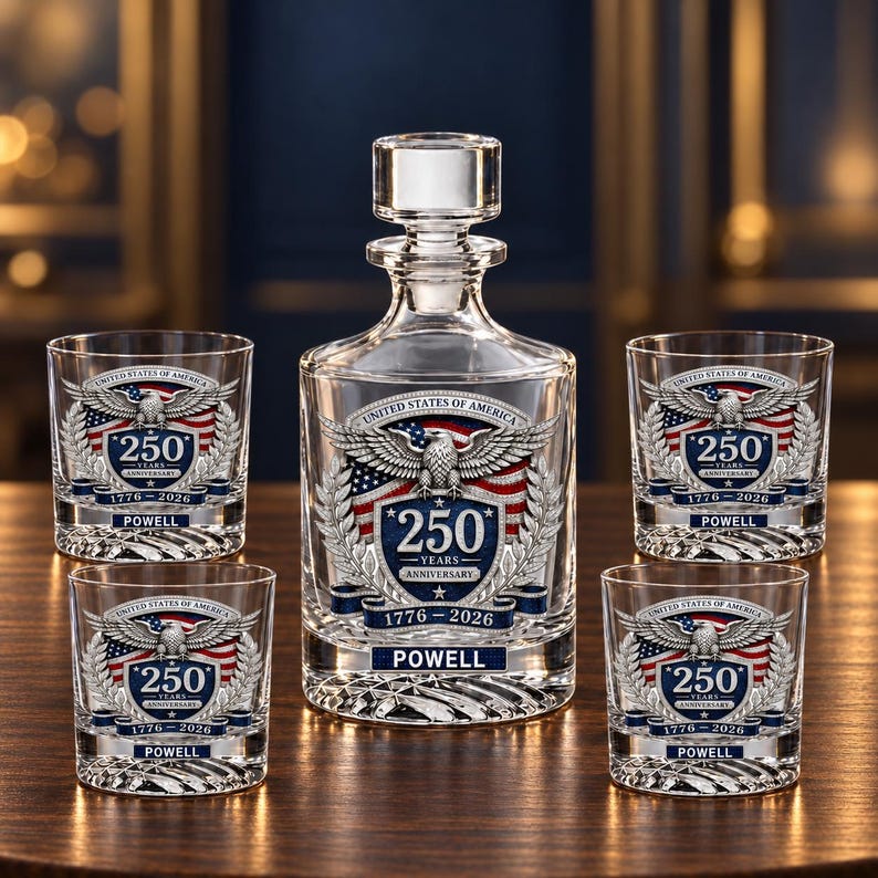 May include: A clear glass decanter and four matching glasses featuring a United States of America 250 years anniversary emblem with an eagle, American flag, and the text 1776-2026 and POWELL. The glassware has a textured base and a clear stopper.