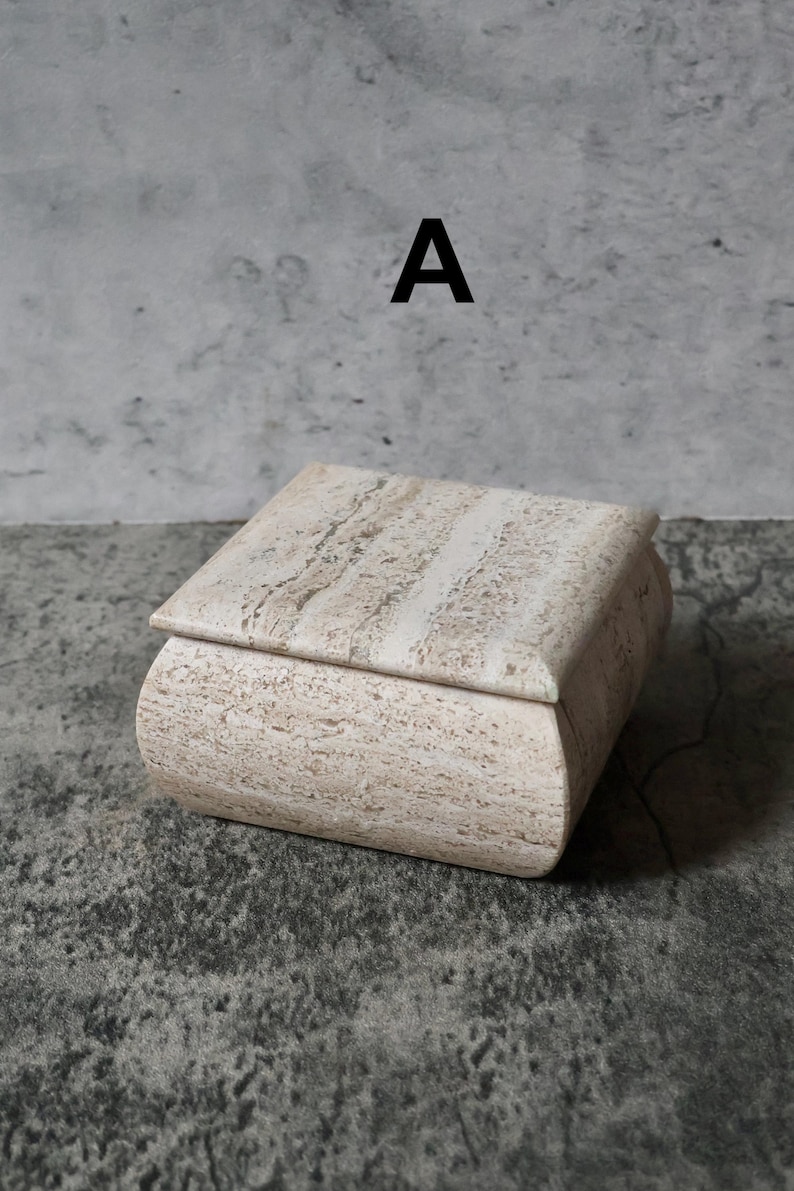 May include: A rectangular, beige stone box with a lid. The box has rounded edges and a natural, textured surface. The letter "A" is printed in black on the background.