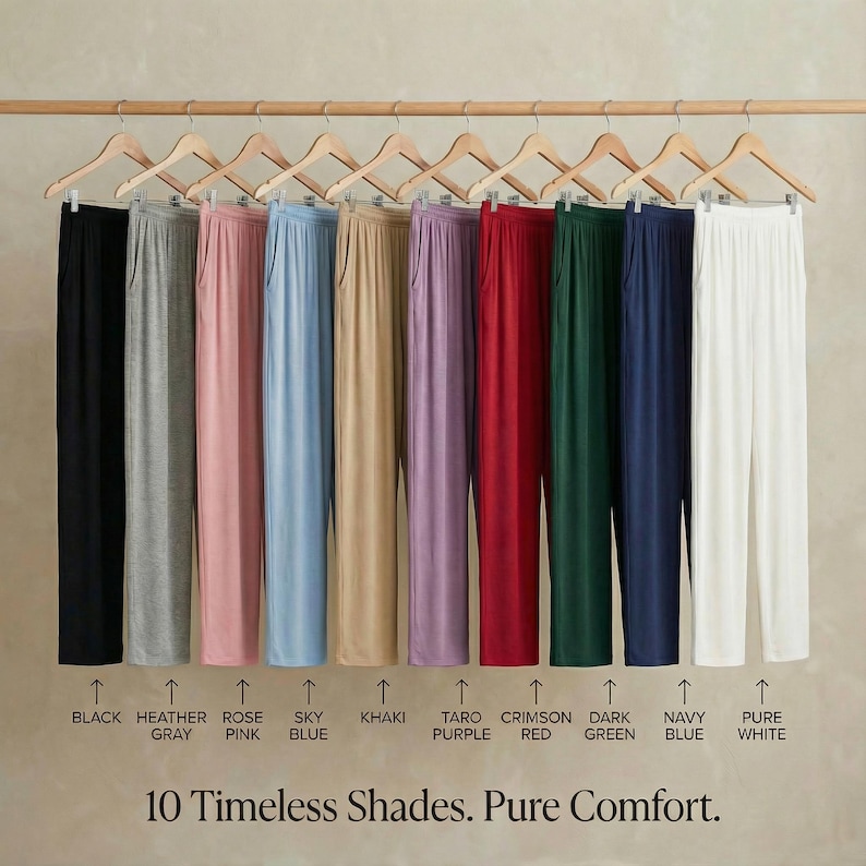 May include: A display of ten pairs of solid-color pants hanging on wooden hangers. Colors include black, heather gray, rose pink, sky blue, khaki, taro purple, crimson red, dark green, navy blue, and pure white. The text reads "10 Timeless Shades. Pure Comfort."