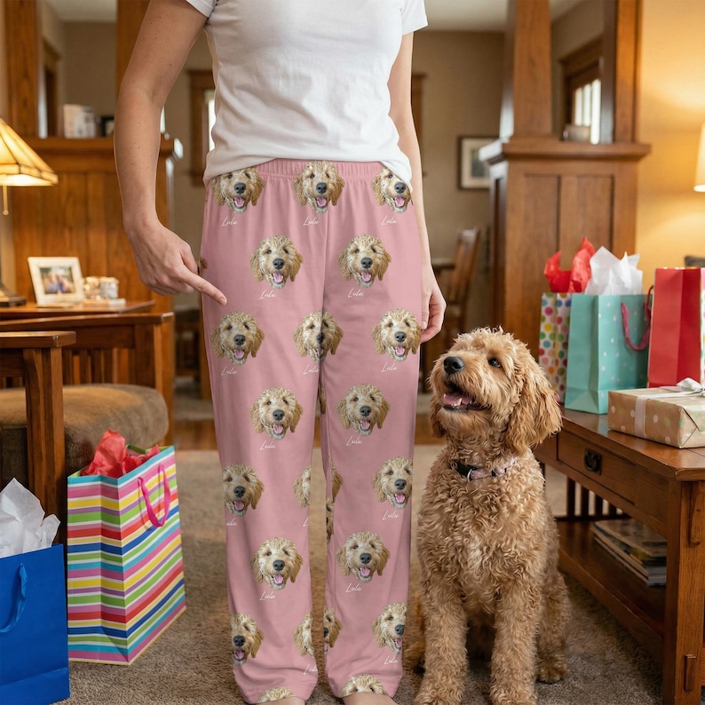 May include: Pink pajama pants featuring a repeating pattern of smiling golden doodle faces. The pants are loose-fitting and have a comfortable, casual style. A golden doodle dog sits nearby. The pajama pants are a unique and personalized gift.