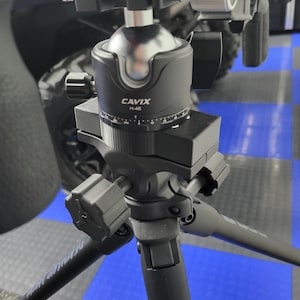 May include: A black tripod with a ball head mount. The ball head has a silver top and a black base with the text "CAVIX H-46". The tripod legs are dark gray and extend from the base.