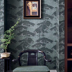 May include: An interior scene featuring a dark green tree-patterned wallpaper, a framed painting, and a black wooden chair with a green cushion. A small bonsai tree sits on a side table. The room has a dark wood floor and a built-in bookshelf.