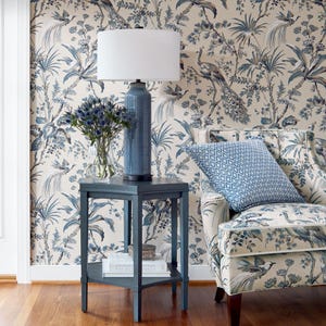 May include: A blue and white floral patterned armchair with a blue and white patterned pillow sits in a room with blue and white floral wallpaper. A blue end table with a white lamp and a vase of blue flowers sits next to the chair.