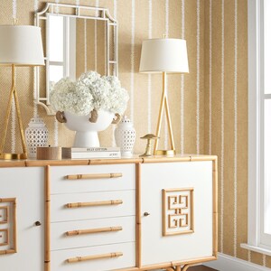 May include: White bamboo dresser with four drawers and a cabinet door. The cabinet door has a decorative geometric design. The dresser has bamboo handles and sits on a woven rug. The dresser is in front of a wall with a beige and white striped wallpaper.