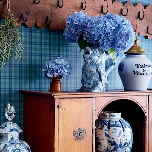 Puede incluir: Un armario de madera con un jarr&oacute;n de porcelana azul y blanco lleno de hortensias azules. El armario tiene un estante con un tarro de porcelana azul y blanco con el texto "Tabac de St. Vincent" en &eacute;l. Hay un jarr&oacute;n de porcelana azul y blanco en el estante inferior.