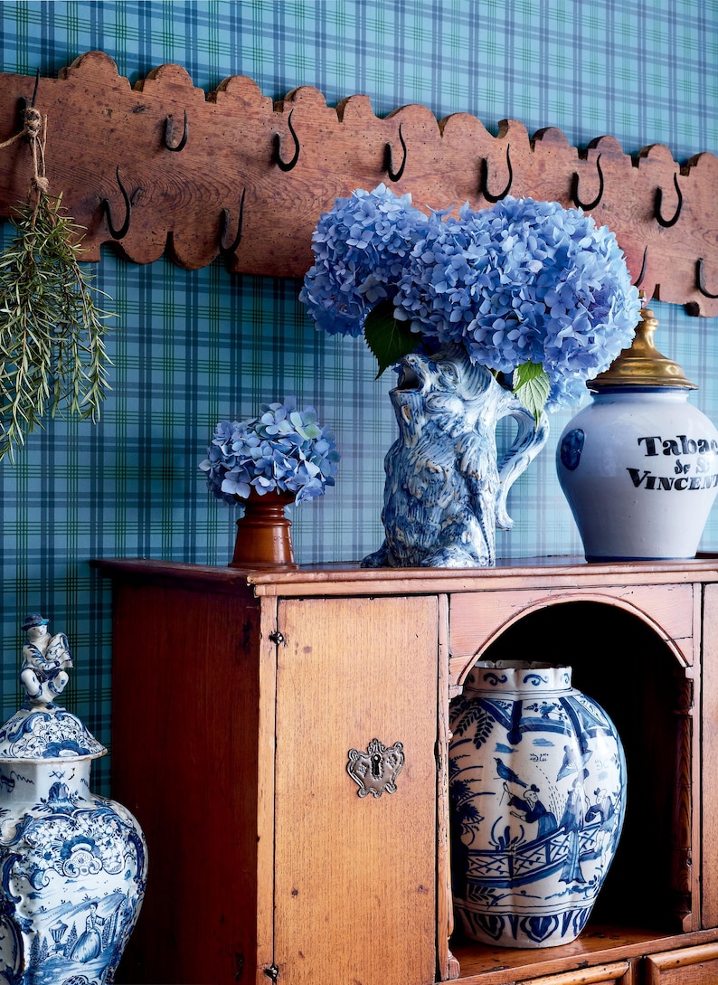 Puede incluir: Un armario de madera con un jarr&oacute;n de porcelana azul y blanco lleno de hortensias azules. El armario tiene un estante con un tarro de porcelana azul y blanco con el texto "Tabac de St. Vincent" en &eacute;l. Hay un jarr&oacute;n de porcelana azul y blanco en el estante inferior.