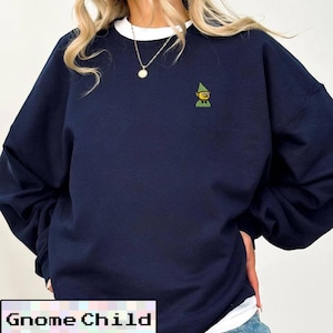 May include: Navy blue sweatshirt with a white crew neck collar. The sweatshirt features a small embroidered gnome graphic on the chest. The text "Gnome Child" is displayed in a white box at the bottom of the image.