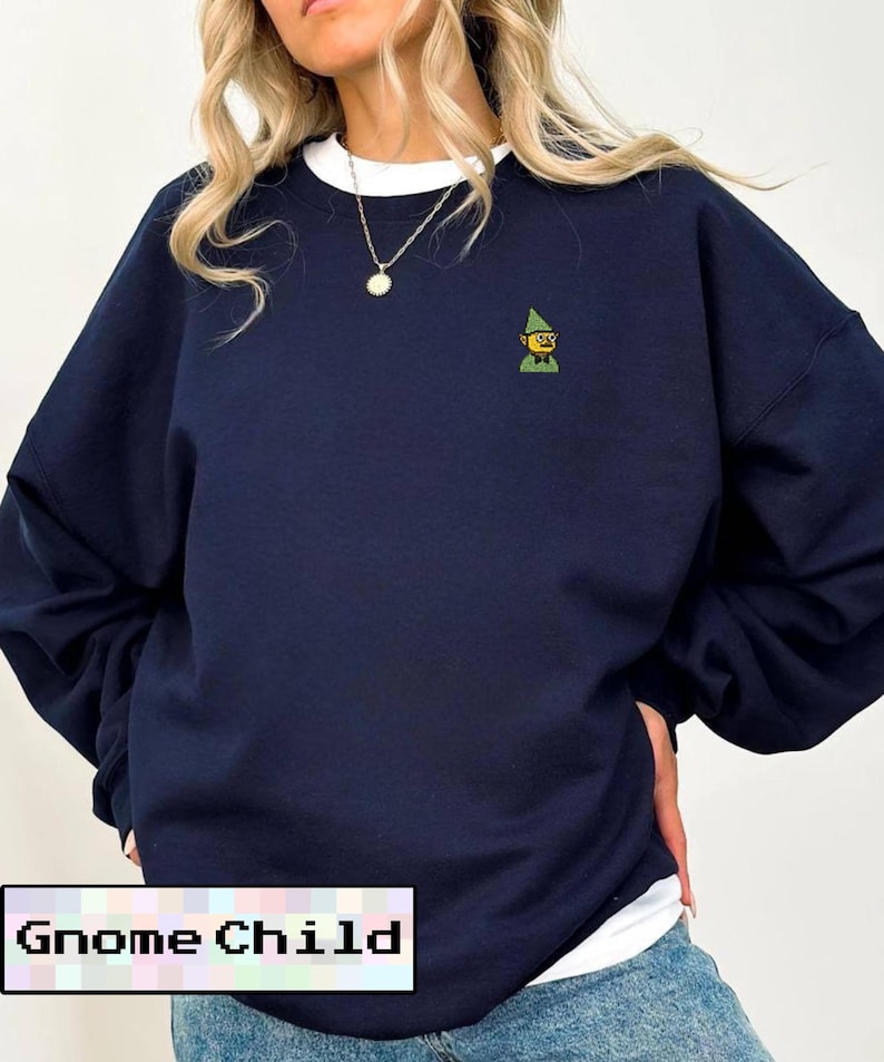 May include: Navy blue sweatshirt with a white crew neck collar. The sweatshirt features a small embroidered gnome graphic on the chest. The text "Gnome Child" is displayed in a white box at the bottom of the image.
