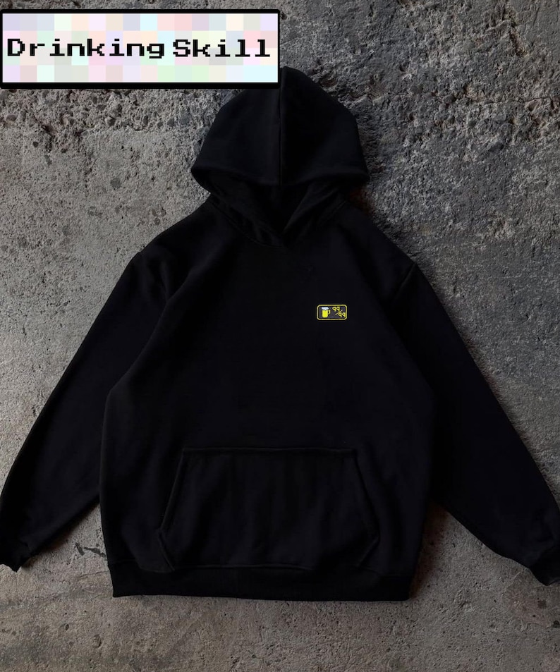 May include: Black hoodie with a front pocket and hood. The text "DRINKING SKILL" is displayed in a white rectangle at the top. A small yellow and black graphic is on the left chest.