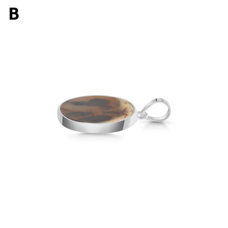 Puede incluir: Un colgante redondo con un engaste de metal plateado pulido. La piedra central es un disco liso y plano con una base de color crema e inclusiones dendr&iacute;ticas de color marr&oacute;n oscuro en forma de &aacute;rbol. Una anilla de metal plateado est&aacute; unida al lateral.