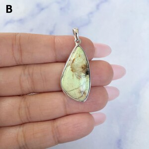Pu&ograve; includere: Un ciondolo a forma di goccia con una pietra verde pallido con inclusioni di matrice marrone e nera, incastonato in una montatura in metallo color argento lucido con un piccolo gancio integrato sulla parte superiore per una catenina.