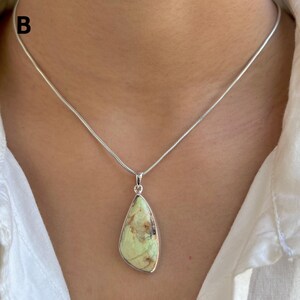 Pu&ograve; includere: Una collana a catena a serpente in argento con un ciondolo a forma di goccia contenente una pietra verde pallido con inclusioni di matrice marrone. La lettera B &egrave; visibile nell'angolo in alto a sinistra. Il ciondolo ha una cornice in argento.