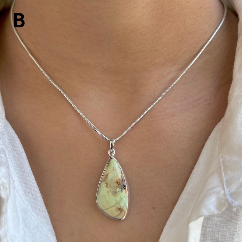 Pu&ograve; includere: Una collana a catena a serpente in argento con un ciondolo a forma di goccia contenente una pietra verde pallido con inclusioni di matrice marrone. La lettera B &egrave; visibile nell'angolo in alto a sinistra. Il ciondolo ha una cornice in argento.