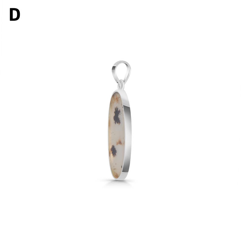 Puede incluir: Un colgante de plata con una piedra de forma ovalada, superficie lisa de color blanco roto e inclusiones oscuras dendr&iacute;ticas con forma de helecho. La piedra est&aacute; engastada en un bisel de plata pulida con una peque&ntilde;a anilla circular.