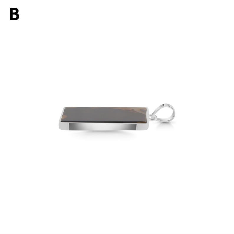 May include: A rectangular pendant featuring a dark brown stone with lighter brown inclusions, set in a polished silver-toned metal frame. The pendant includes a silver-toned metal bail attached to one side for hanging on a chain or cord.