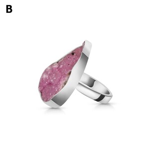 May include: A silver ring featuring a large, irregular-shaped pink gemstone. The gemstone has a rough, textured surface with a mix of pink and white hues. The ring band is a polished silver.