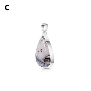 May include: A teardrop-shaped pendant featuring a smooth, white stone with dark, dendritic fern-like inclusions. The stone is set in a polished silver-toned metal frame with a matching silver-toned bail at the top. The letter C is visible.