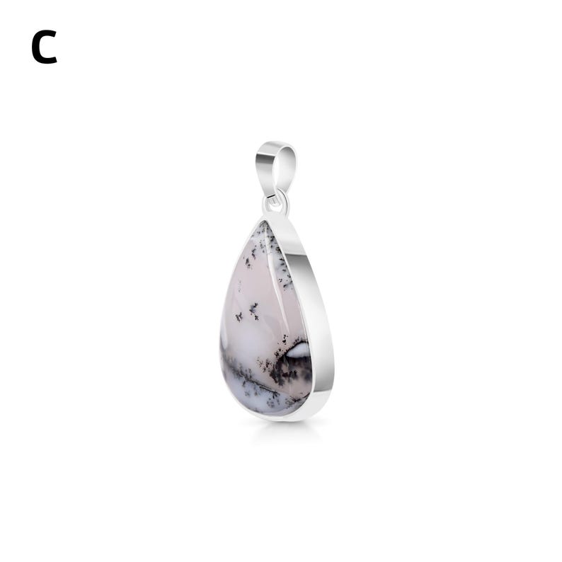 May include: A teardrop-shaped pendant featuring a smooth, white stone with dark, dendritic fern-like inclusions. The stone is set in a polished silver-toned metal frame with a matching silver-toned bail at the top. The letter C is visible.