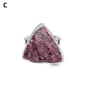 May include: A silver ring featuring a triangular, rough-cut gemstone. The stone is a mix of pink and gray hues, set within a polished silver band. The ring's design highlights the natural texture and color variations of the stone.