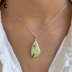 Pu&ograve; includere: Una collana in argento con un ciondolo a forma di goccia contenente una pietra verde pallido. La pietra presenta inclusioni naturali marrone scuro ed &egrave; incastonata in una montatura in argento liscia. Il ciondolo pende da una catenina sottile.