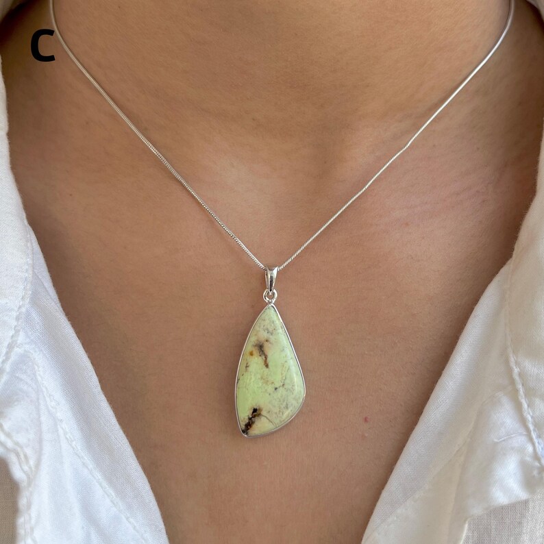 Pu&ograve; includere: Una collana in argento con un ciondolo a forma di goccia contenente una pietra verde pallido. La pietra presenta inclusioni naturali marrone scuro ed &egrave; incastonata in una montatura in argento liscia. Il ciondolo pende da una catenina sottile.