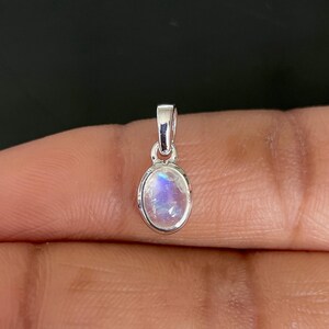 May include: A small, oval pendant with a silver-coloured bail. The pendant features a polished, iridescent moonstone with blue and white hues. The gemstone is set in a silver bezel.