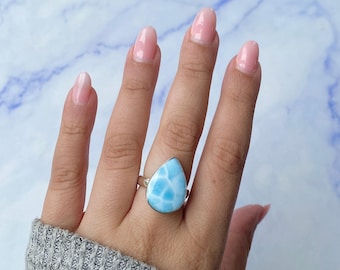 May include: A teardrop-shaped Larimar gemstone ring set in a polished silver band. The stone features a distinct sky-blue color with white, cloud-like marbling patterns throughout its surface, creating a smooth, polished appearance on the finger.