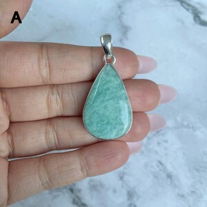 May include: A teardrop-shaped pendant featuring a smooth, light green stone with subtle white veining, set in a polished silver-toned metal frame with a matching silver-toned bail at the top for attachment to a chain or cord.